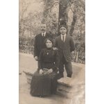 Carte photo - femme assise sur un banc avec 2 hommes debout derri�re
